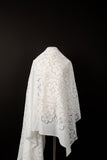 A white laser-cut lace fabric, featuring a pattern combining trefoil shapes and geometric squares.