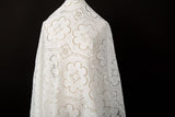A white laser-cut lace fabric, featuring a pattern combining trefoil shapes and geometric squares.
