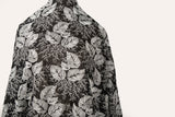 A black and white embroidered cotton fabric, with a stylized pattern of large leaves and coral, resembling a woodcut print.
