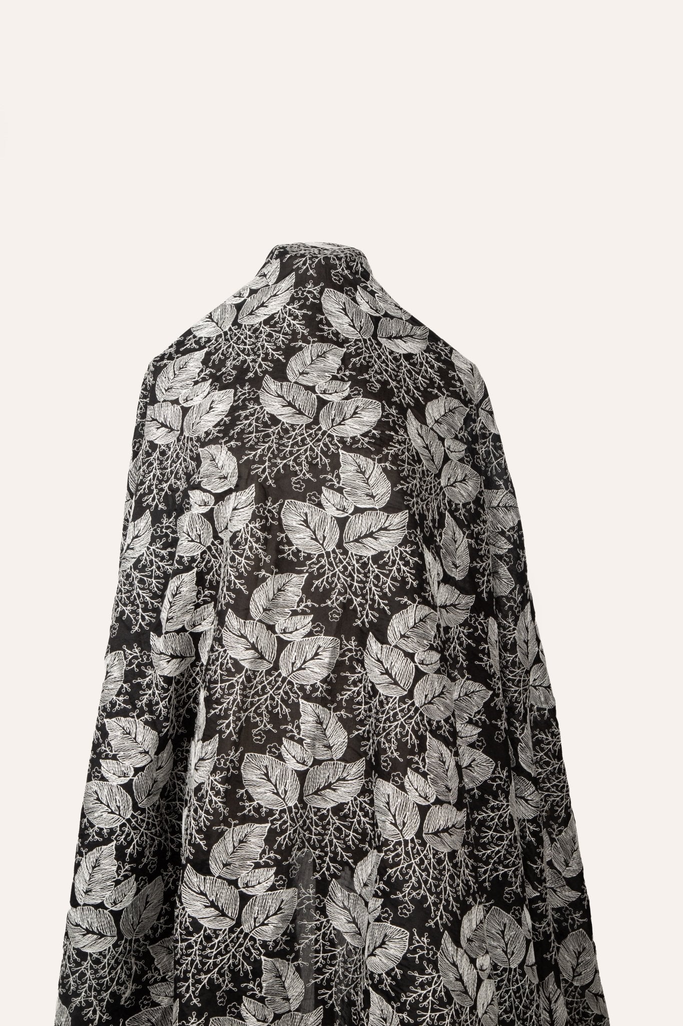 A black and white embroidered cotton fabric, with a stylized pattern of large leaves and coral, resembling a woodcut print.