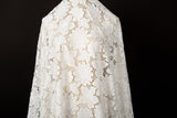 A white laser-cut lace fabric, featuring an all-over pattern of stylized daisies.