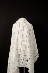 A white laser-cut fabric, featuring a regular grid pattern with floral embroidery inside each square.
