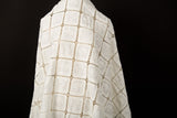 A white laser-cut fabric, featuring a regular grid pattern with floral embroidery inside each square.