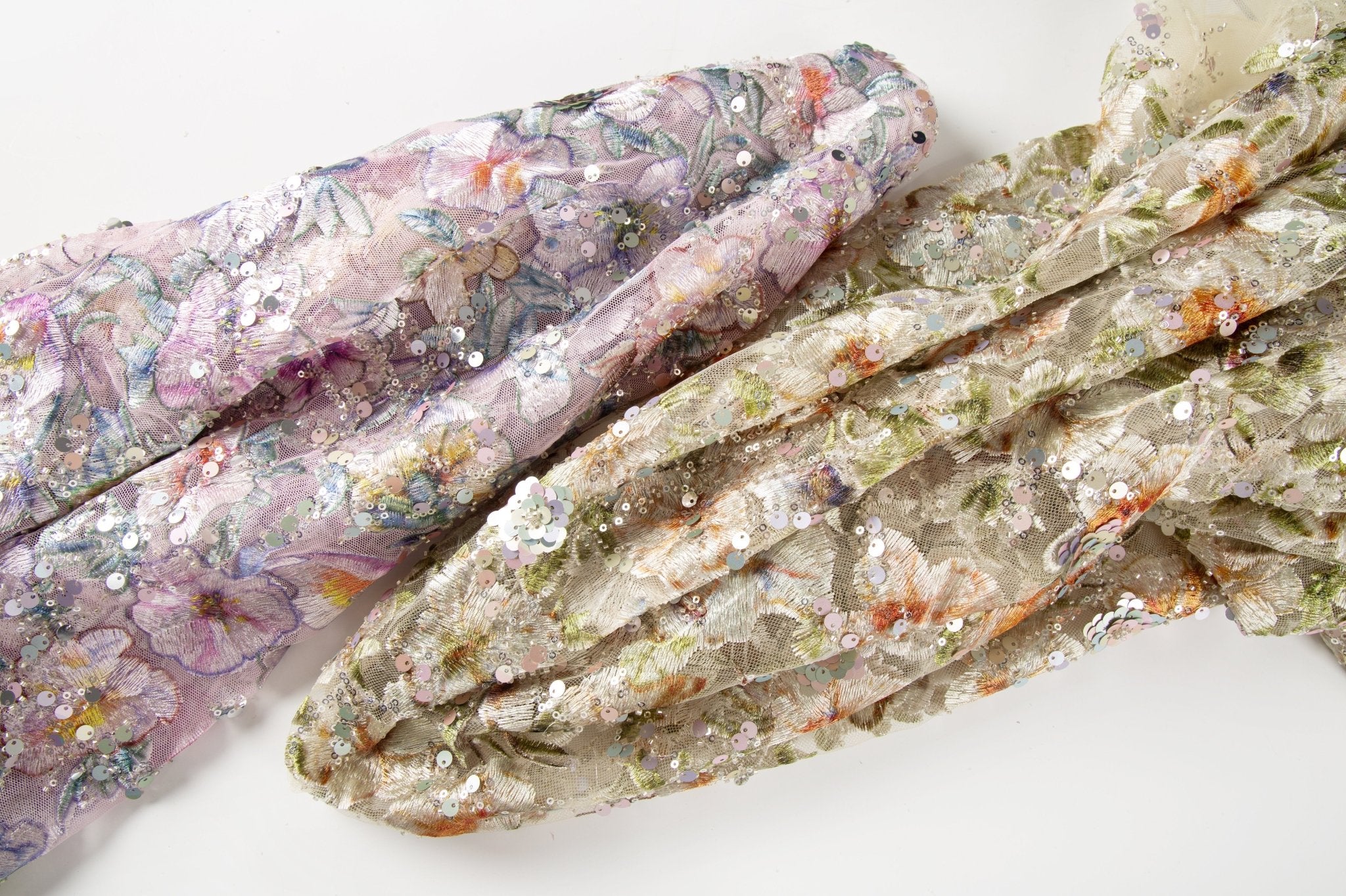 A dense, painterly floral sequin and thread embroidery fabric in a warm palette of greens and oranges.
    A dense, painterly floral sequin and thread embroidery fabric in a cool palette of purples and blues.