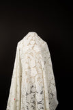 A white laser-cut lace fabric, featuring large-scale, swirling paisley and floral motifs.