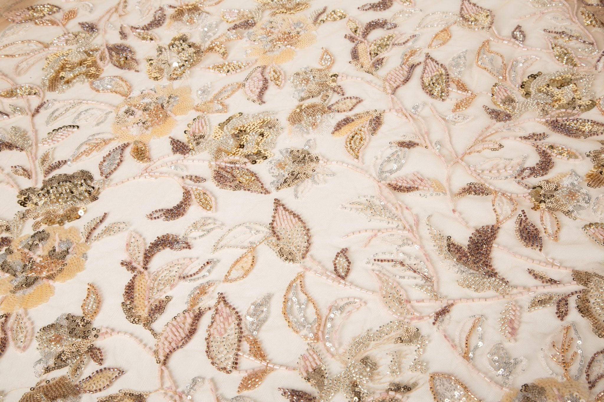 A luxurious beaded embroidery fabric, with a dense, trailing floral vine pattern in a warm rose gold and pink palette.