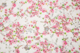 A fine embroidery fabric on white tulle, with a pattern of pink cherry blossom branches and shimmering sequins.