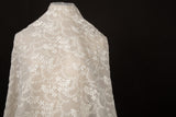 An ivory-white flat embroidery organza fabric, with a graceful, scalloped or arched garland pattern made of small flowers.