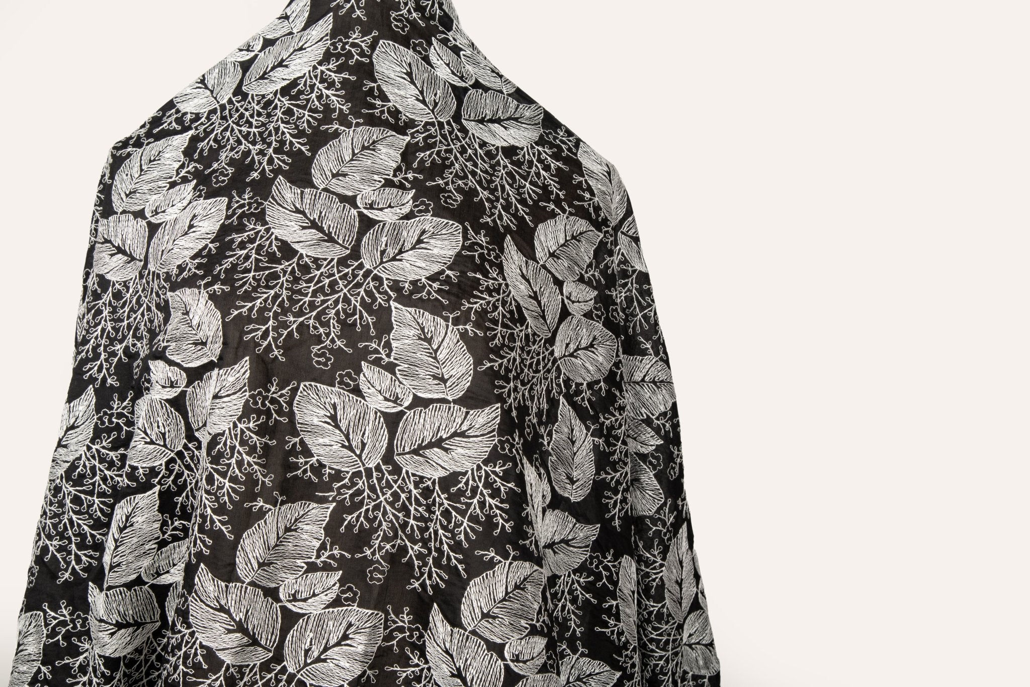 A black and white embroidered cotton fabric, with a stylized pattern of large leaves and coral, resembling a woodcut print.
