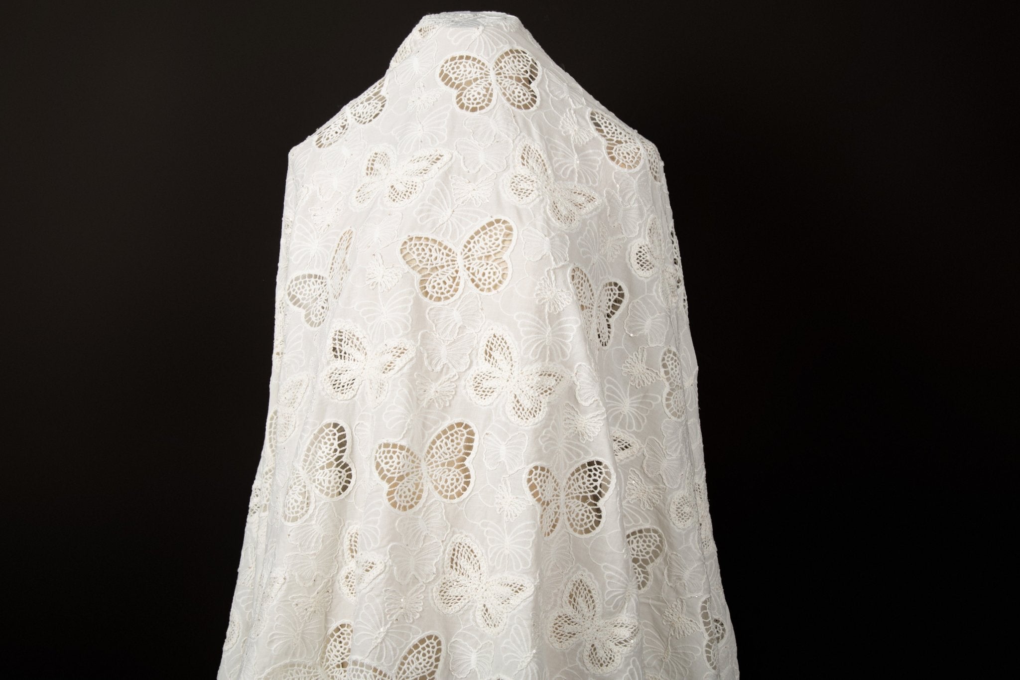 A white laser-cut lace fabric, featuring an all-over pattern of butterflies in various sizes.