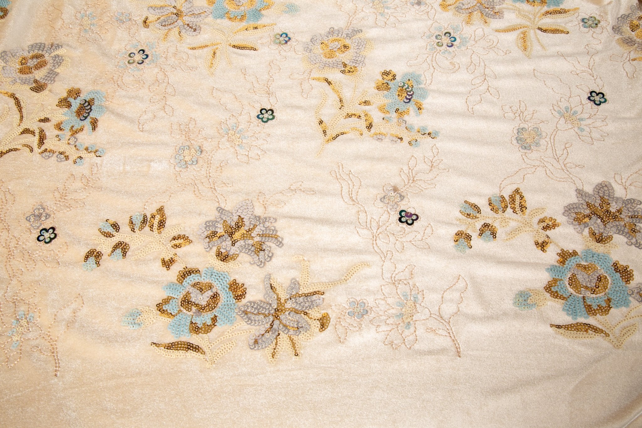 A sequin floral embroidery fabric on a cream velvet base, with blue and gold motifs.
