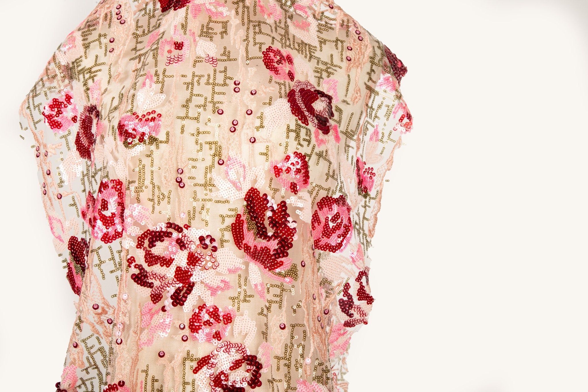 A sequin embroidery fabric on nude mesh with red-toned florals over bronze geometric patterns.

