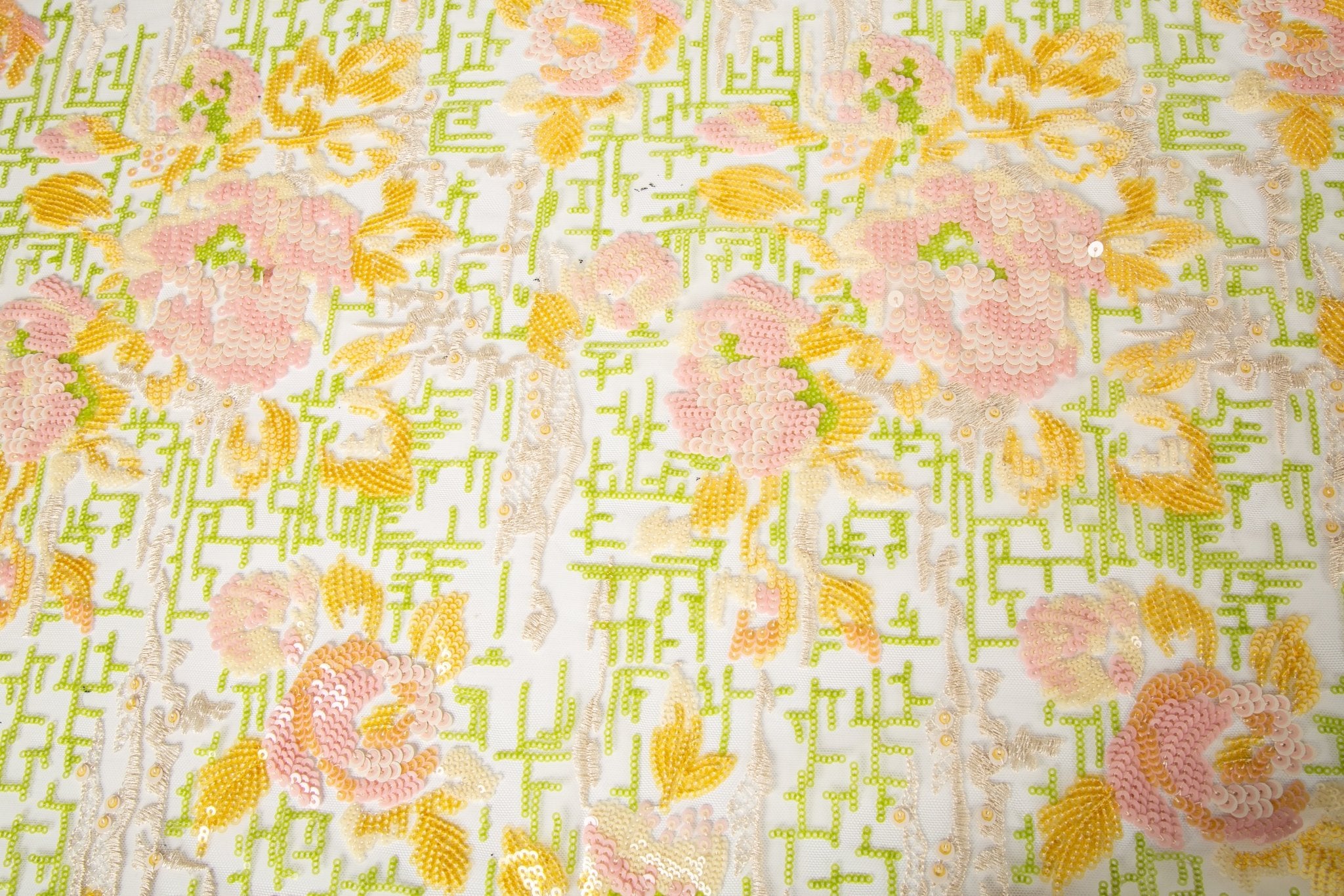 A sequin embroidery fabric on white mesh with yellow-pink florals over green geometric patterns.
