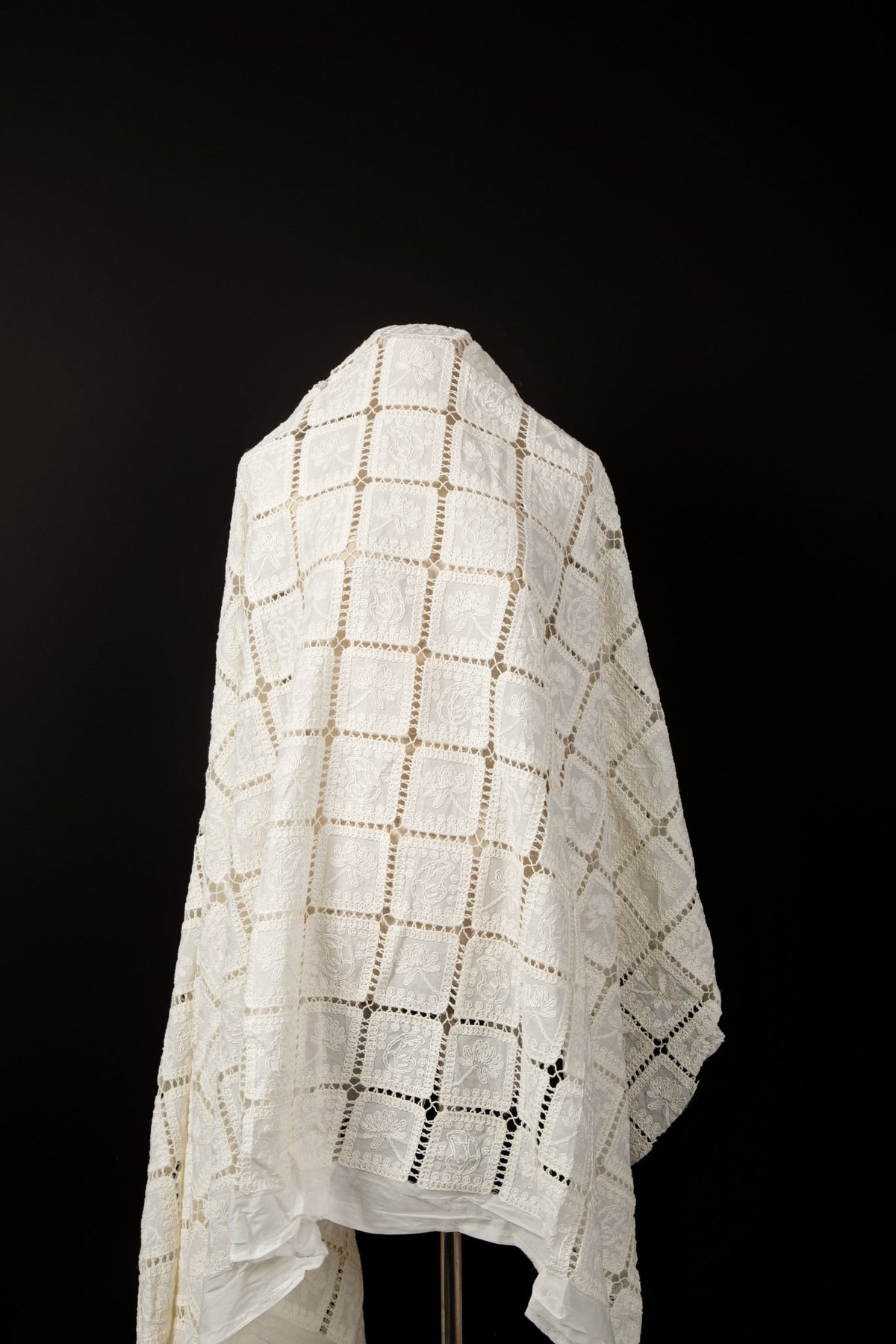  A white laser-cut fabric, featuring a regular grid pattern with floral embroidery inside each square.