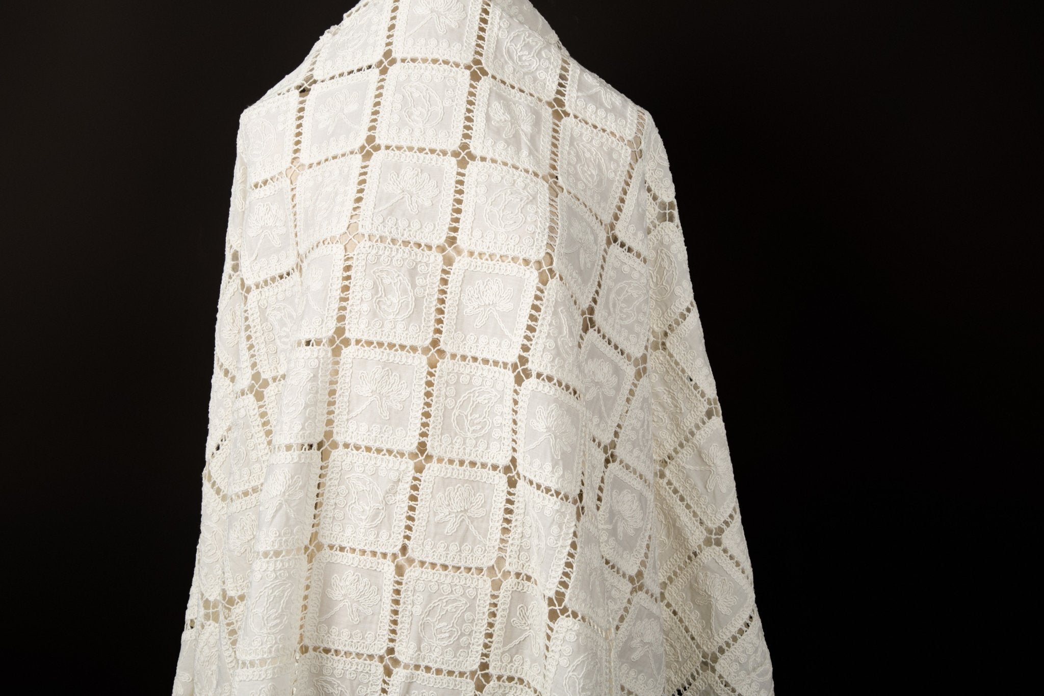  A white laser-cut fabric, featuring a regular grid pattern with floral embroidery inside each square.