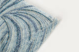 A blue and silver hand-beaded fabric, with an abstract, flowing pattern resembling water currents or mineral strata.
