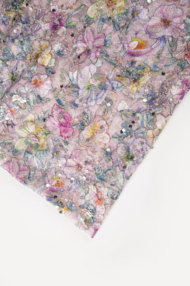 A multi-color floral embroidery fabric on a pale lavender mesh base, with a pattern made of embroidery thread, sequins, and black beads.