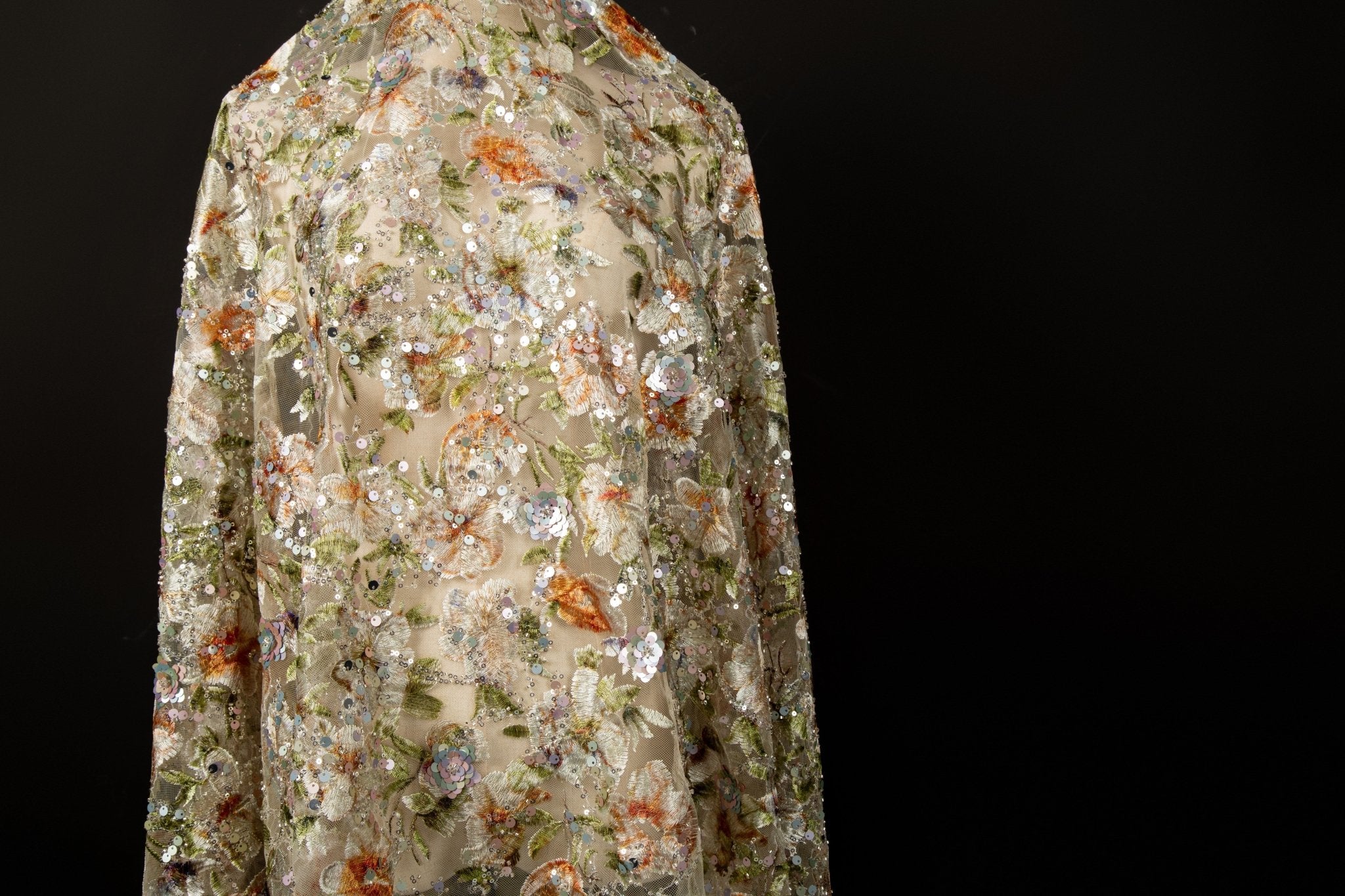 A dense, painterly floral sequin and thread embroidery fabric in a warm palette of greens and oranges.
