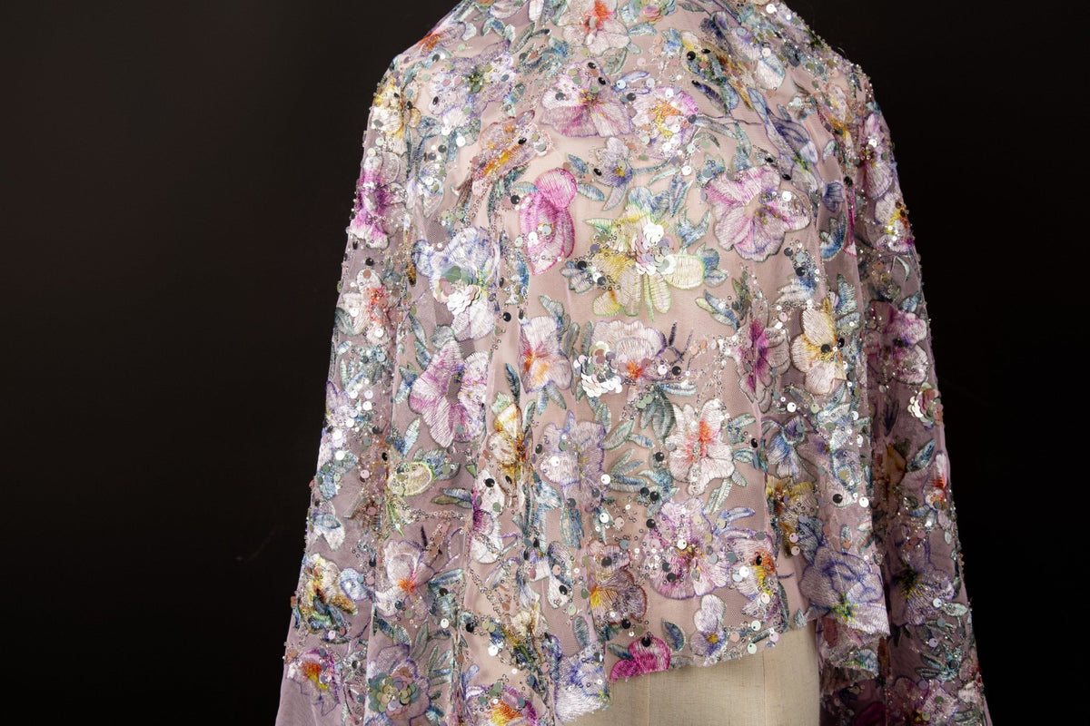 A dense, painterly floral sequin and thread embroidery fabric in a cool palette of purples and blues.

