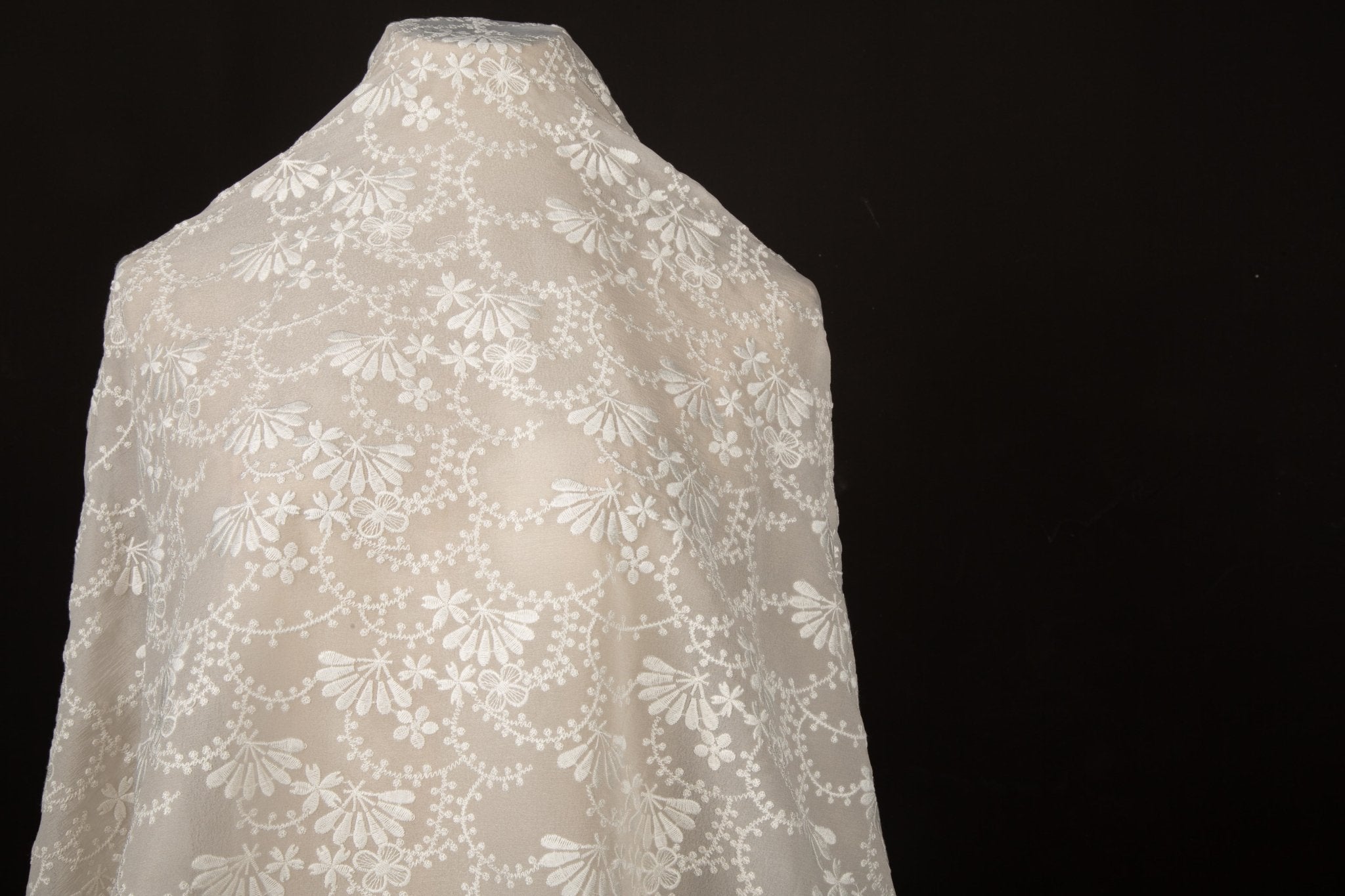 An ivory-white flat embroidery organza fabric, with a graceful, scalloped or arched garland pattern made of small flowers.
