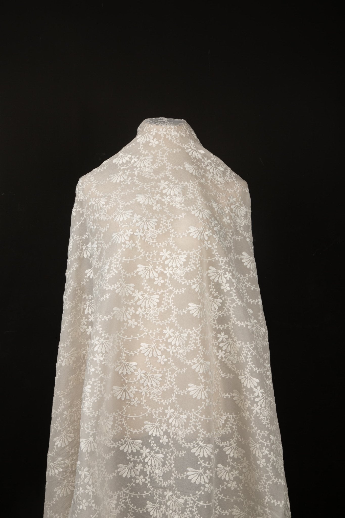 An ivory-white flat embroidery organza fabric, with a graceful, scalloped or arched garland pattern made of small flowers.
