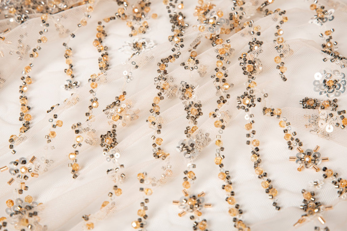 A fine beaded embroidery fabric, with a cascading stardust pattern of vertical lines in champagne gold and pewter.