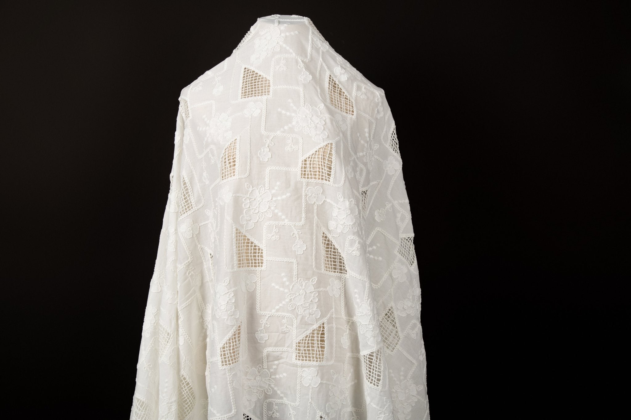 A white laser-cut embroidery fabric, with a pattern of geometric cut-out squares and white floral embroidery.