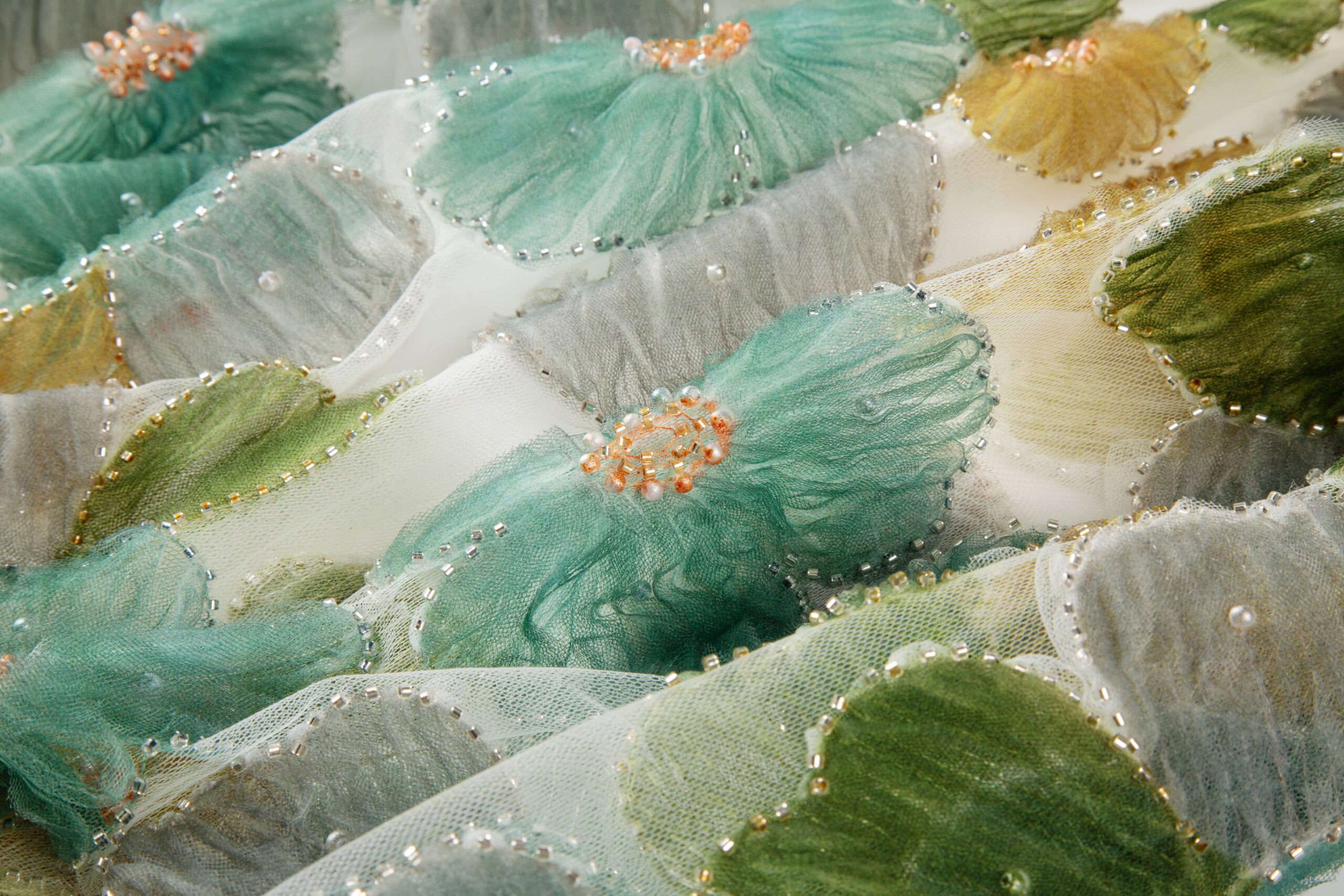 3D flower pattern made of ruffled green mesh tape with bead clusters, sewn on sheer fabric.